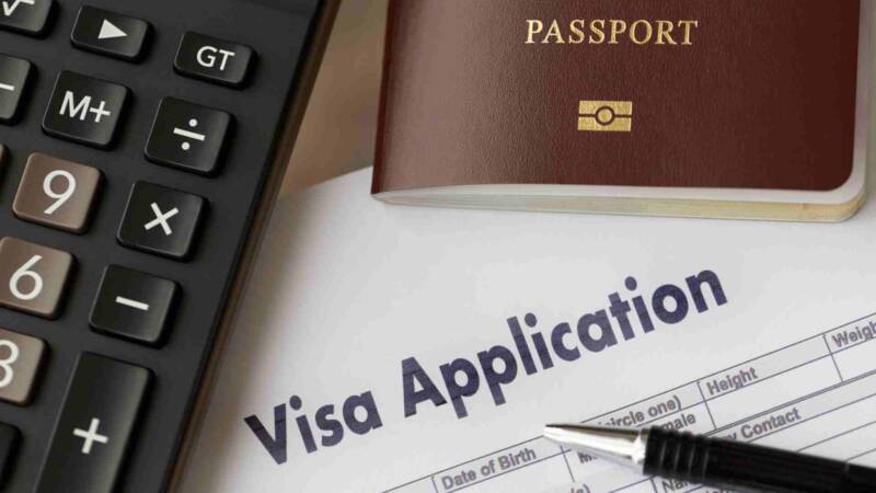 A passport with a visa application form, a pen and keyboard