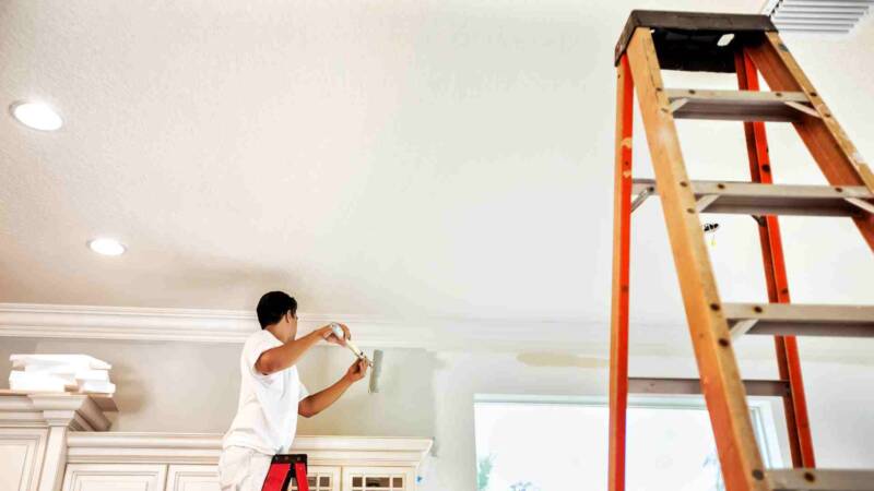 A painter painting a white house ceiling with a stair