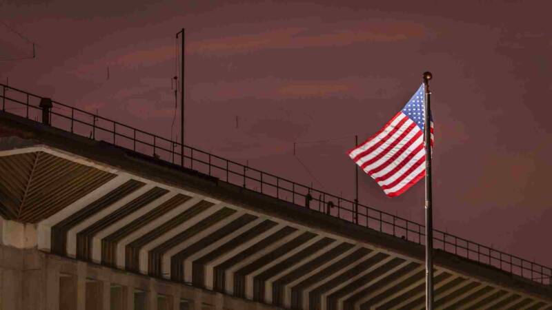 A US flag standing high besides a bridge in sunset
