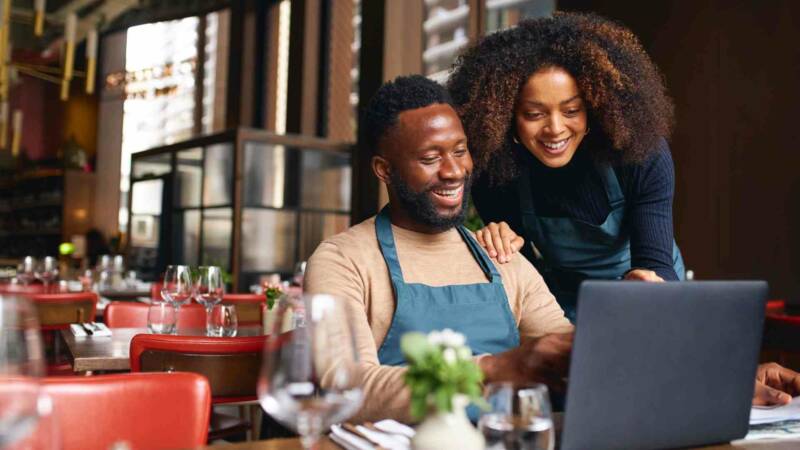Both men and women smiling in front of the computer because of successfully buying an existing business