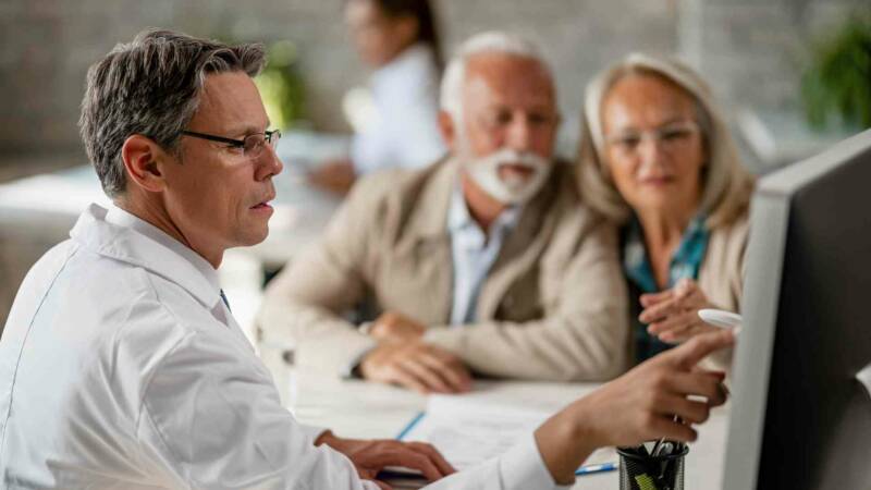 A doctor is talking to an elderly couple in front of a monitor