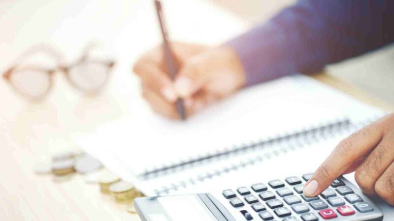 A franchisee calculating franchise cost and fees with a pen, paper, and calculator